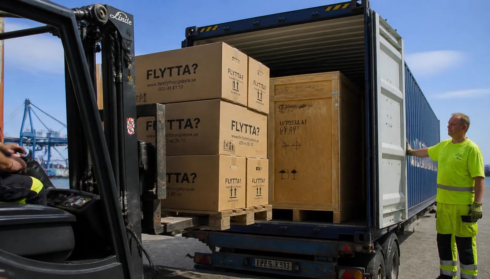 Märkta flyttkartonger och en träback lastas i sjöcontainer i hamn vid utlandsflytt från Stockholm