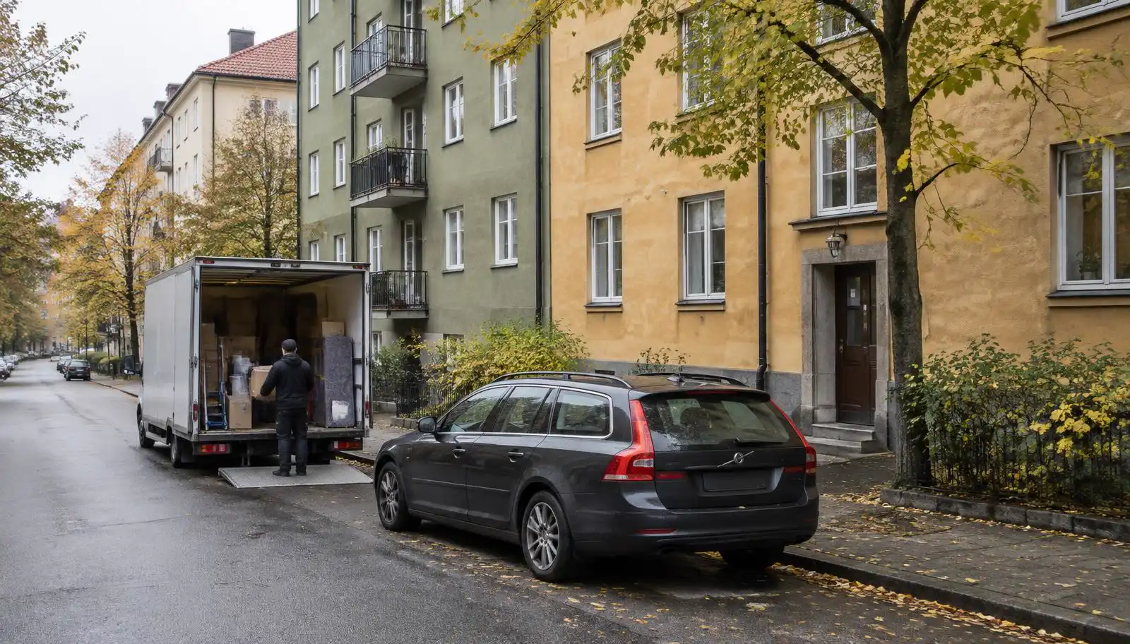 Privatbil parkerad vid trottoaren bredvid en flyttbil som lastas på en gata i Stockholm en höstdag